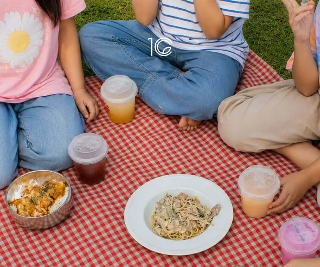 Food and iced drinks laid out on a checked picnic mat on the grass