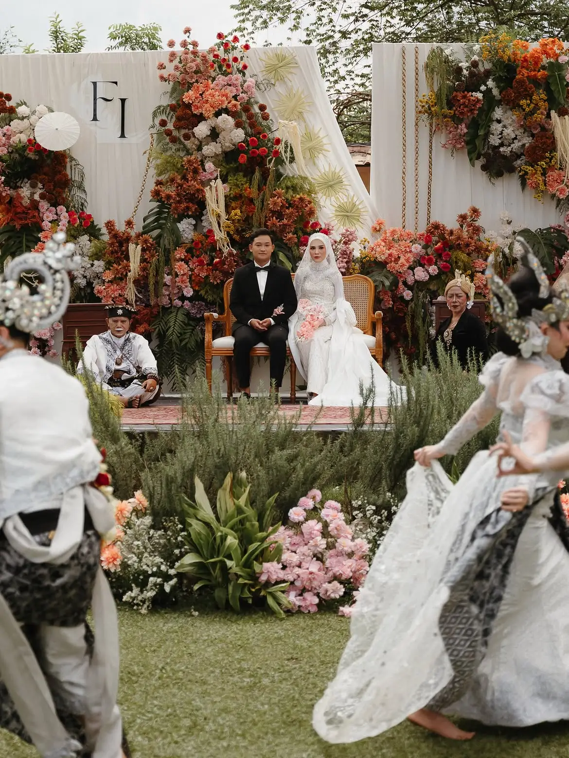 The floral reception stage on the lawn with the couple seated and dancers performing